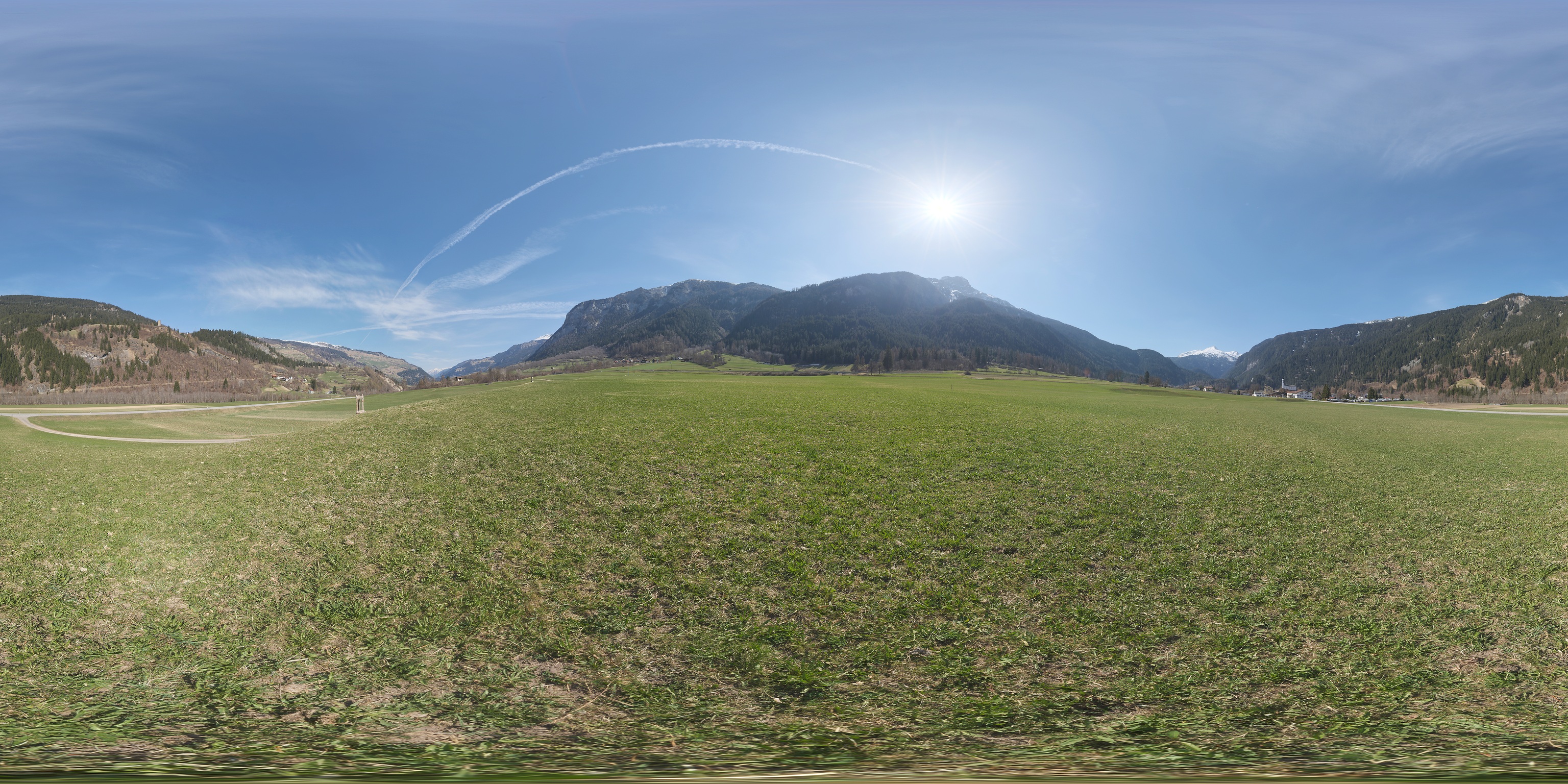 Panoramic photograph of a green field surrounded by mountain slopes.