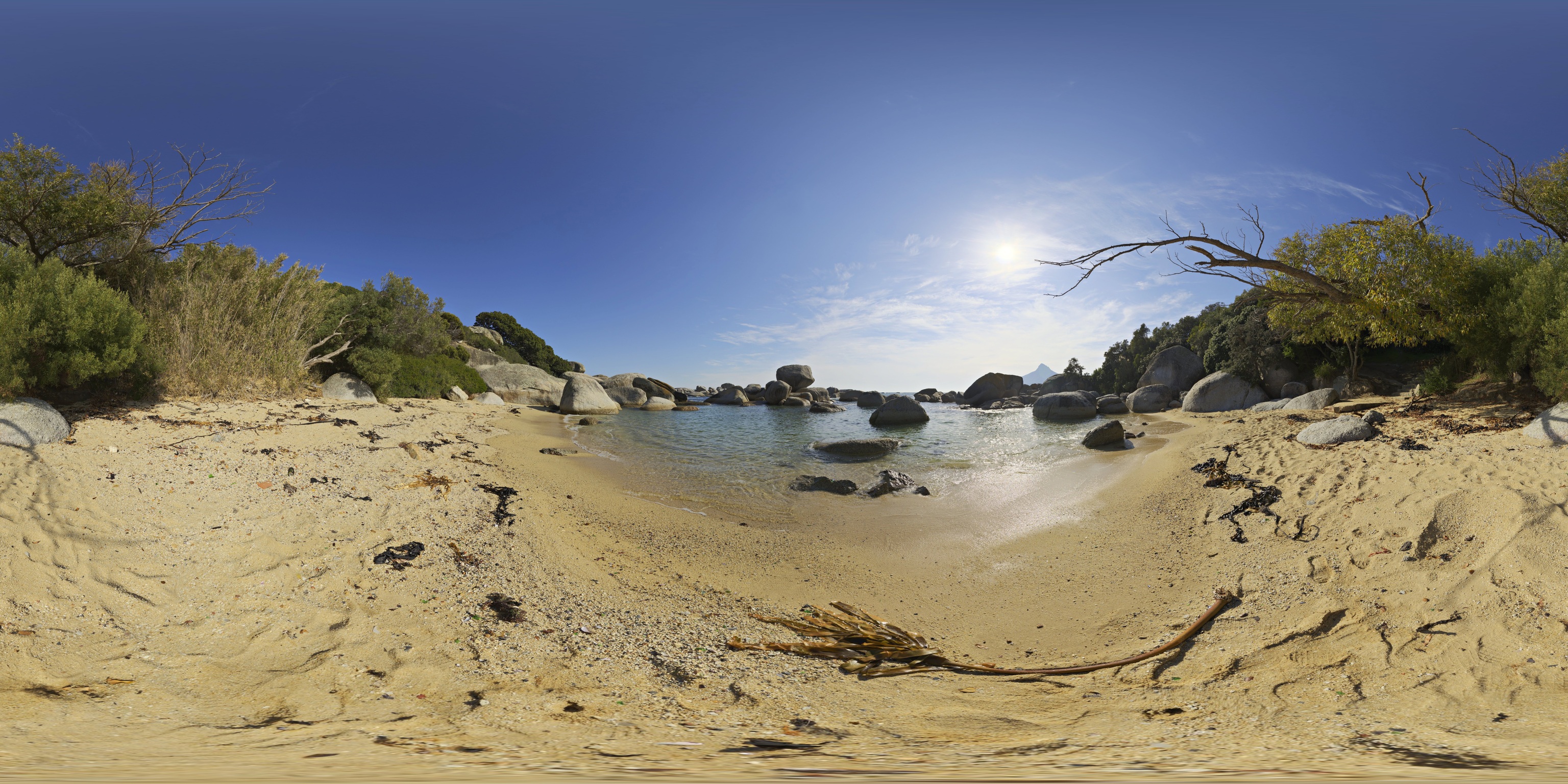 Panoramic photograph of a rocky sandy beach and blue water.